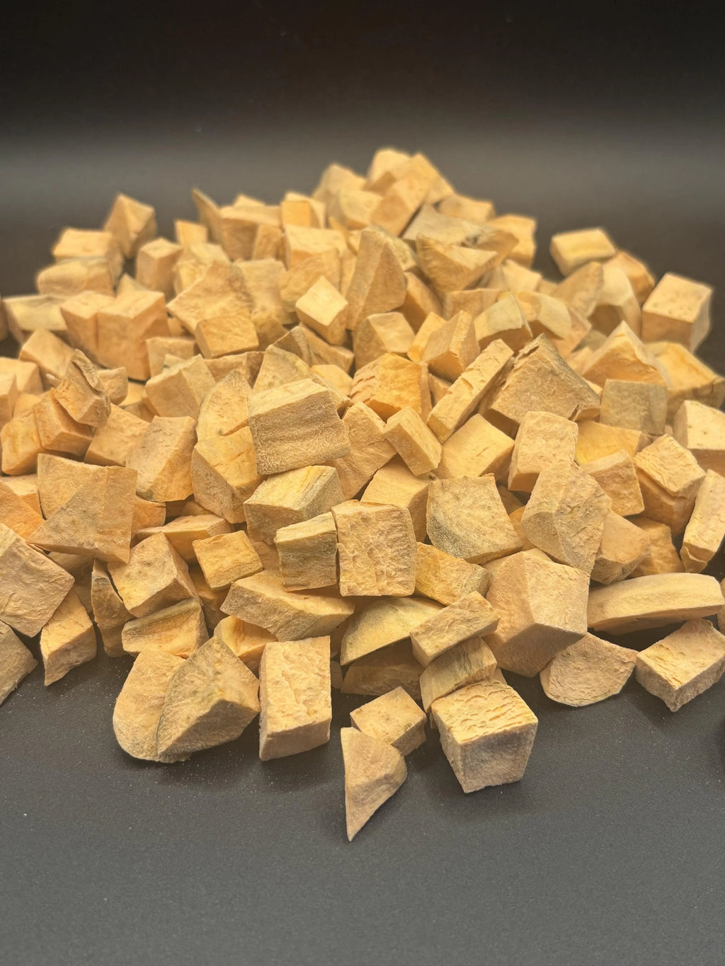 Pile of irregularly cut dried yellow root vegetable pieces on dark surface