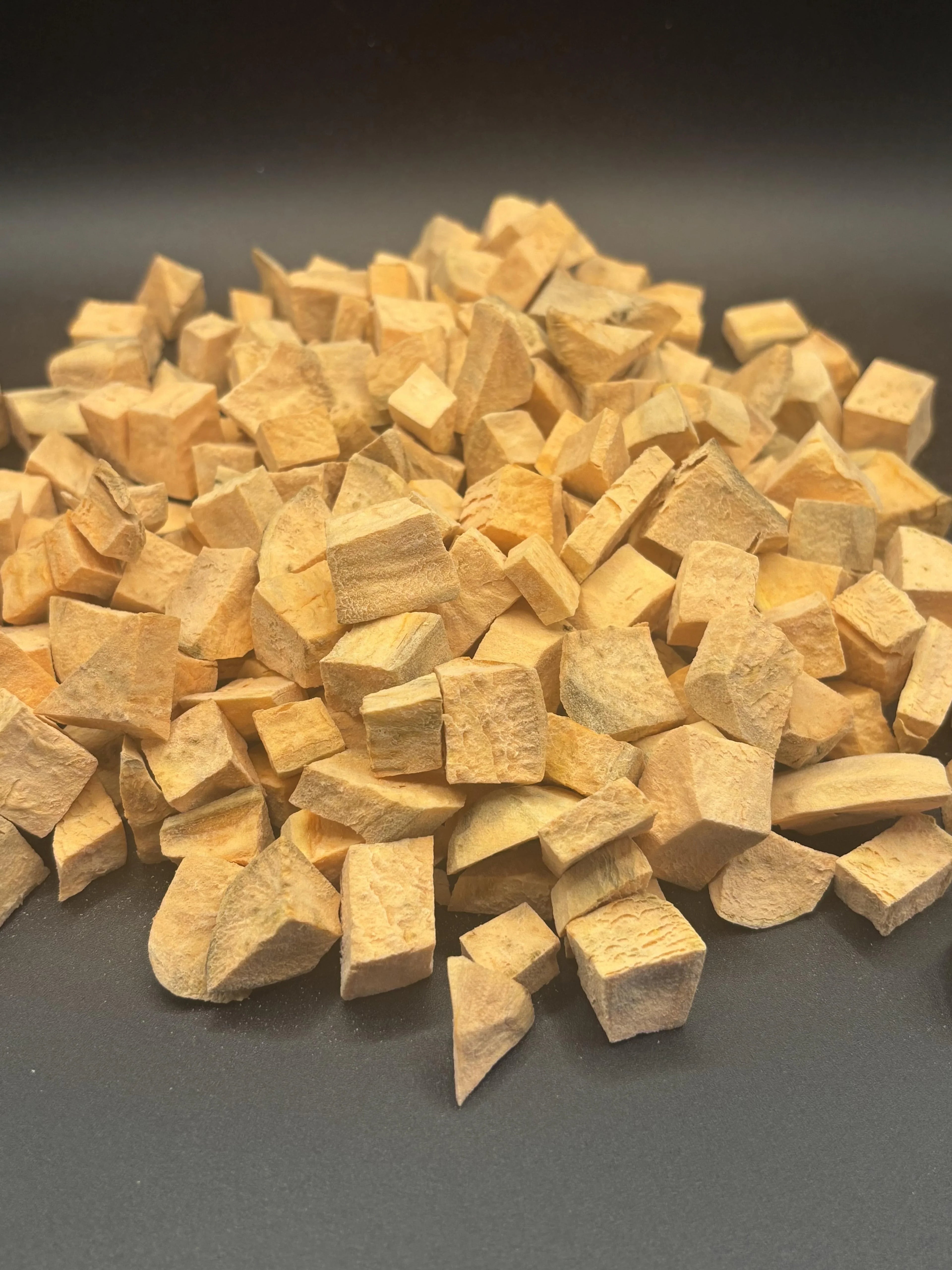 Pile of irregularly cut dried yellow root vegetable pieces on dark surface