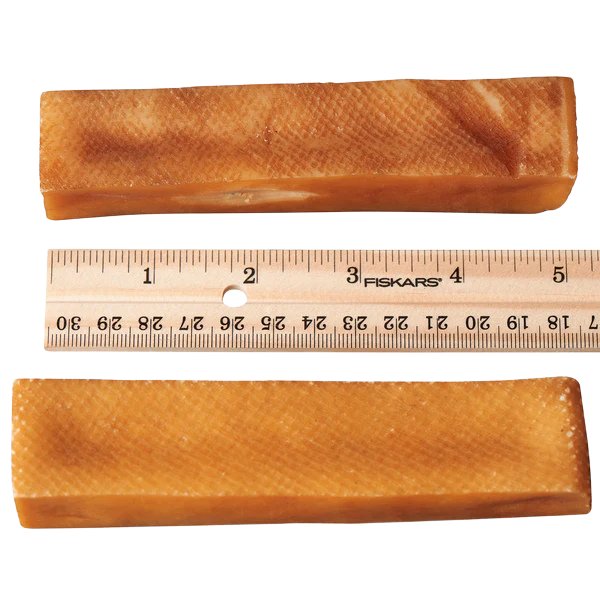 Two dog churpi cheese chews with a Fiskars ruler showing their dimensions on a white background.
